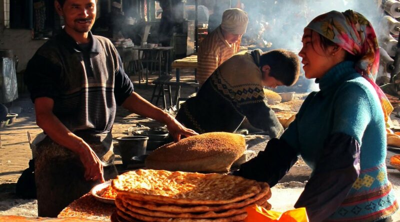 A street kitchen maybe in China, where a man and a womadn are making delicious looking bread and pizza-like pies.